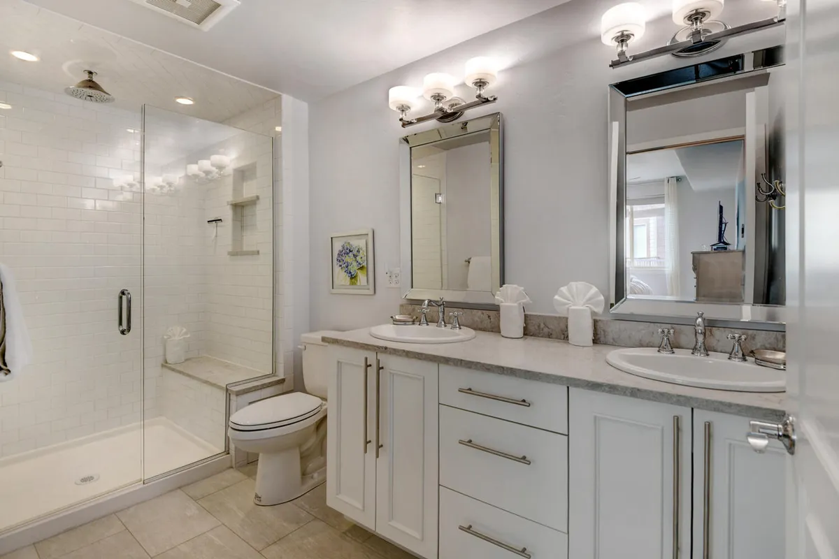 A modern bathroom with a glass shower enclosure, double sink vanity, large mirrors, and sleek lighting. The space feels refreshing and spa-like, ideal for self-care and pampering.