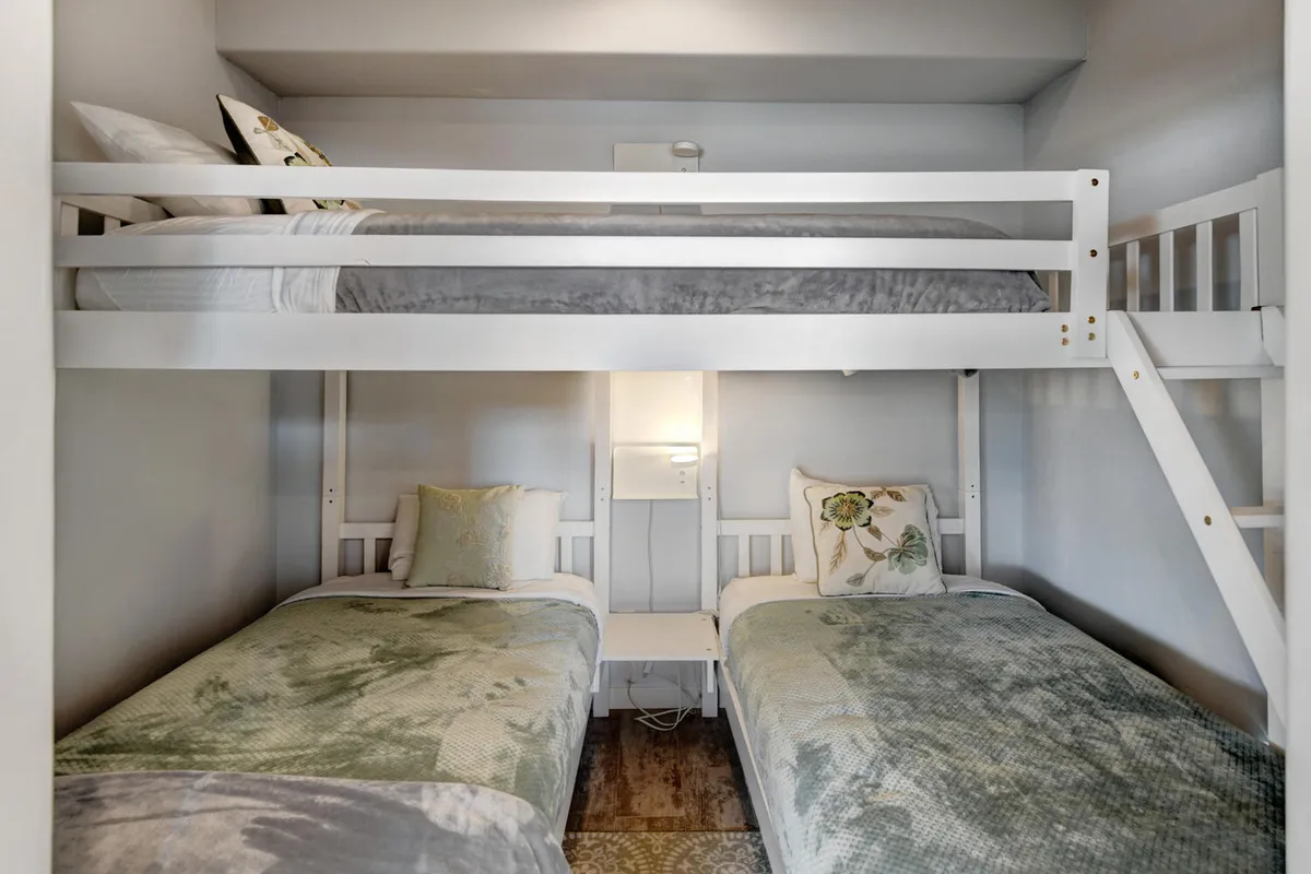 A set of bunk beds with decorative pillows and a nightstand create a playful yet restful sleeping space, ideal for kids or flexible arrangements. The room’s soft colors and textures add to its welcoming ambiance.