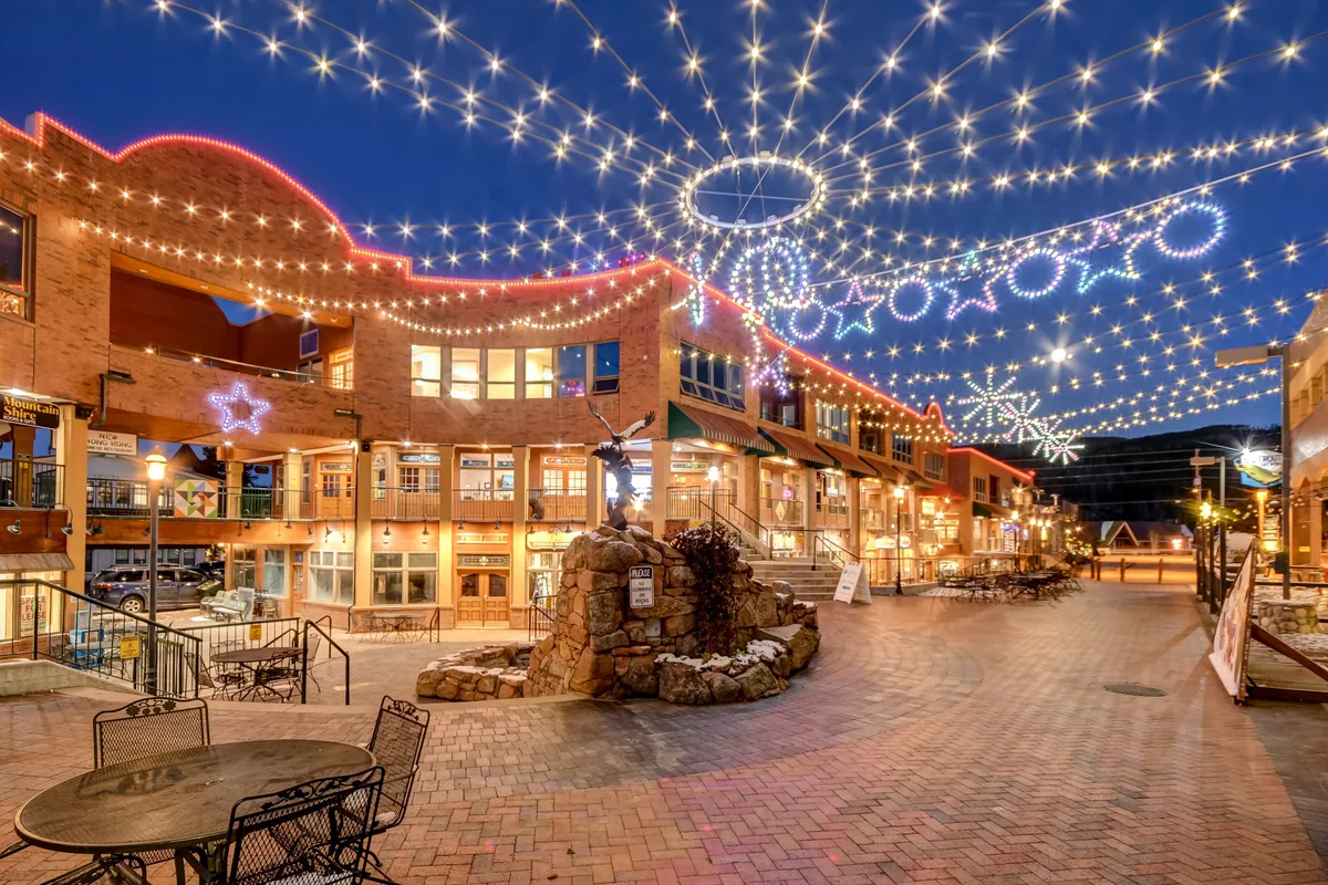 An exterior scene filled with twinkling string lights and festive decorative stars, featuring stone fountains, outdoor seating, and a brick walkway. The atmosphere is joyful and celebratory, suggesting a vibrant community perfect for strolls, dining, or attending local events with your dog.