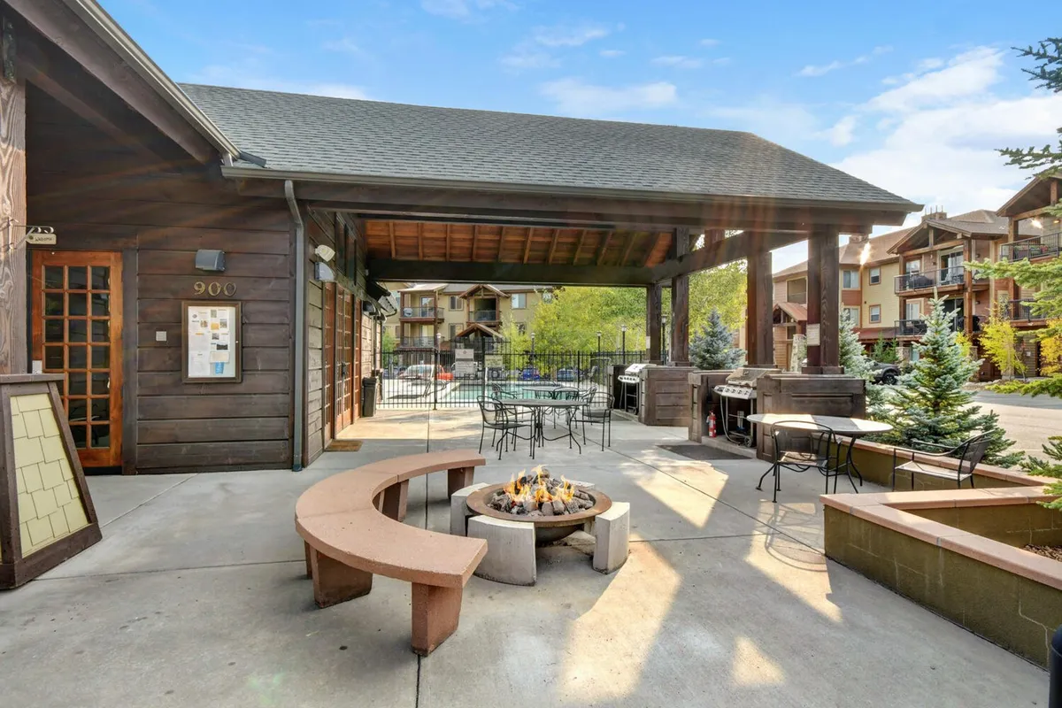 An exterior shot showing a communal fire pit, seating area, grill, and building facade surrounded by greenery. The setup is ideal for group gatherings, outdoor dining, and evening relaxation under the stars.