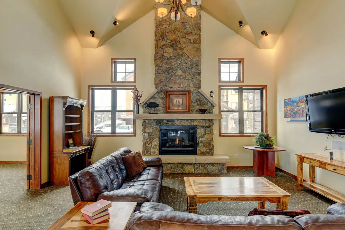 A cozy living room complete with a striking stone fireplace, large panoramic windows, a plush leather sofa, and a wooden coffee table. The space feels warm, stylish, and is ideal for socializing or quiet relaxation.