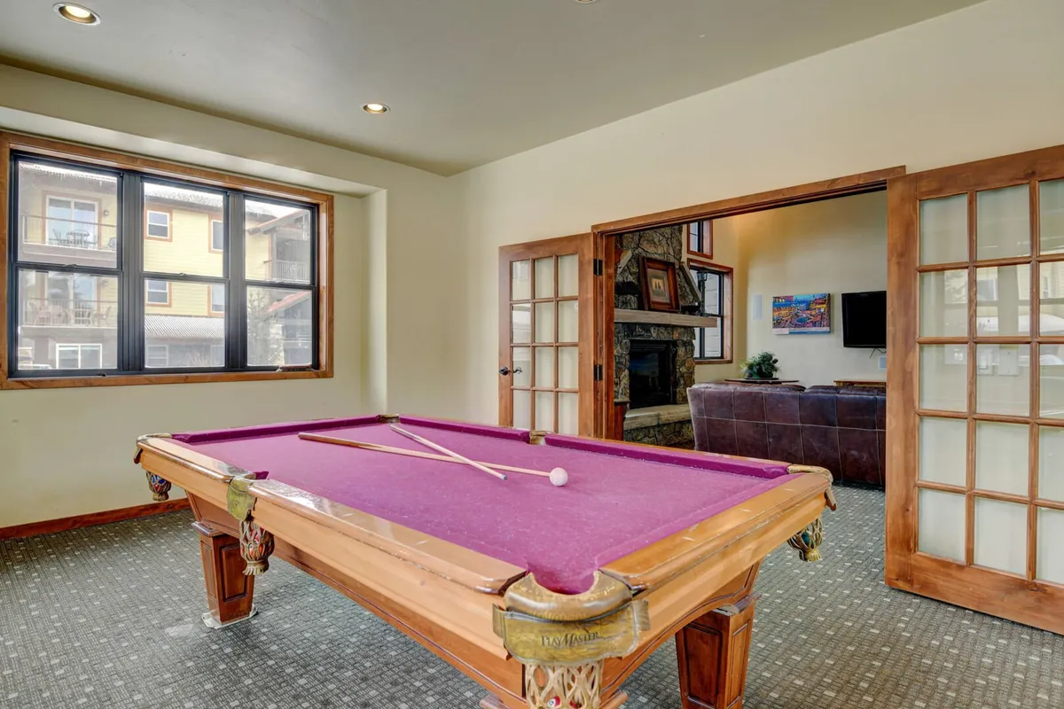A vibrant game room featuring a pool table, large windows that flood the space with light, and a modern fireplace. The atmosphere is lively and social, ideal for unwinding or friendly competition after a day of adventure.