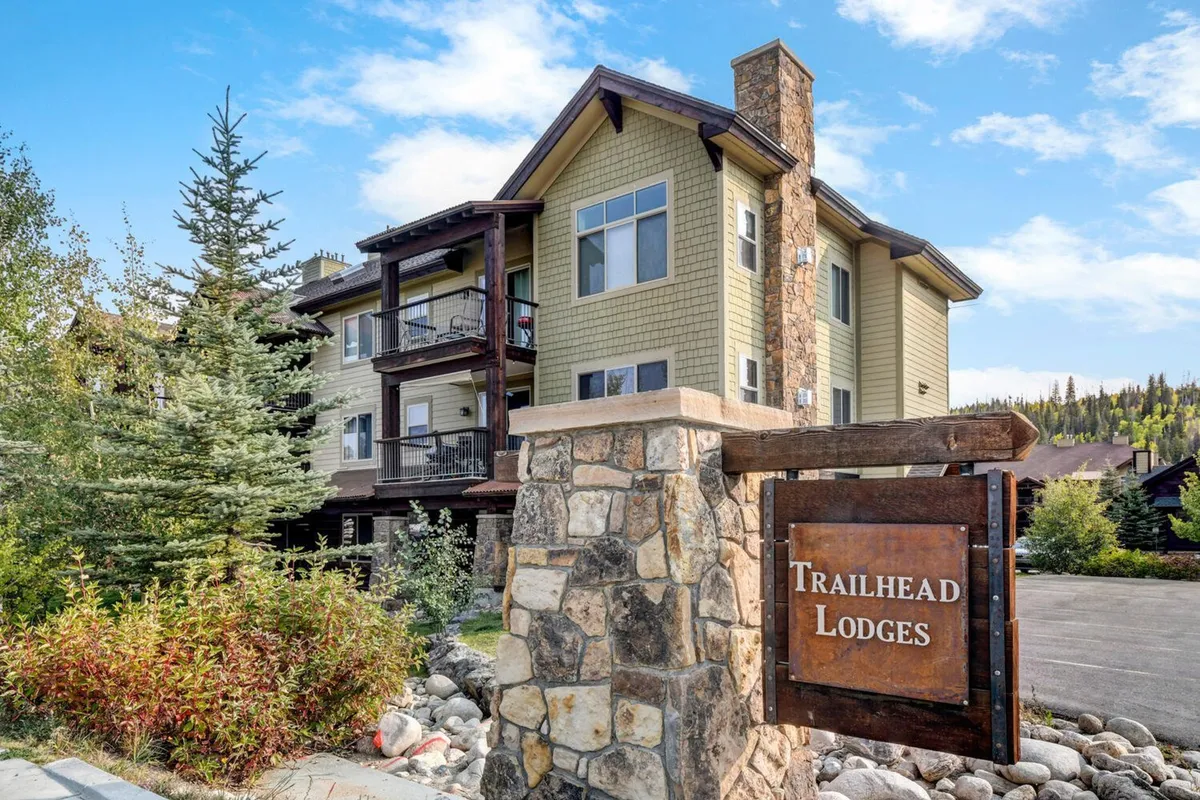 This image features the condo complex's stone entrance sign, wooden balconies, and lush surrounding greenery. The inviting facade and visible balconies indicate a welcoming environment with direct access to nature and outdoor adventures.