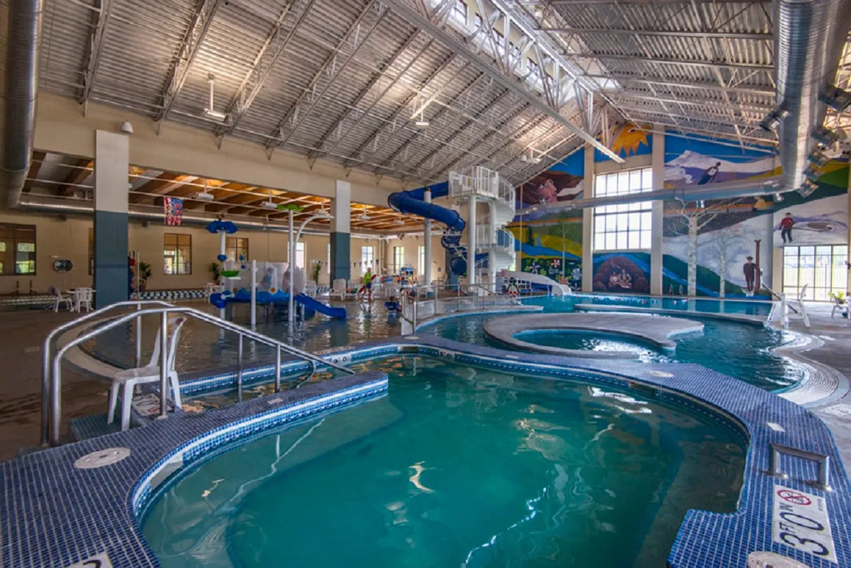 A lively interior scene from the nearby Rec Center featuring colorful water slides, swimming pools, and playful murals, with children and families enjoying water play.